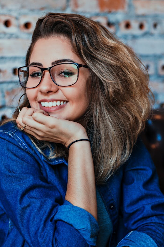 services-01 A young woman wearing glasses and denim, smiling in an indoor setting.