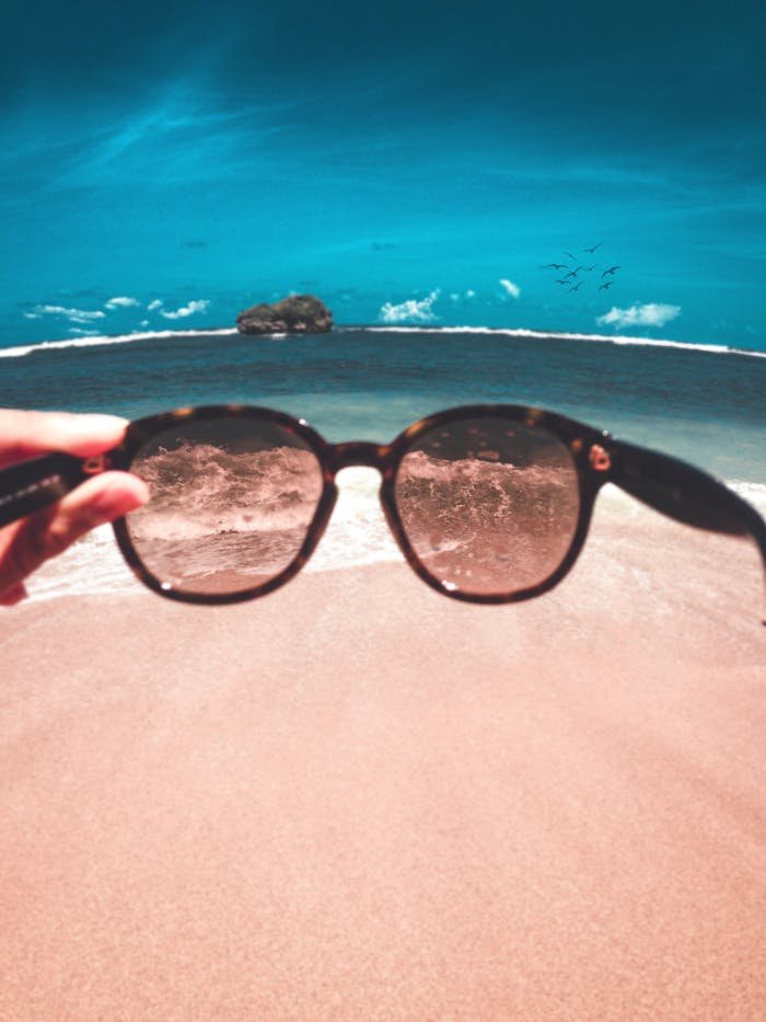 Hand holding sunglasses with a beach and ocean view. Captures summer relaxation vibes.