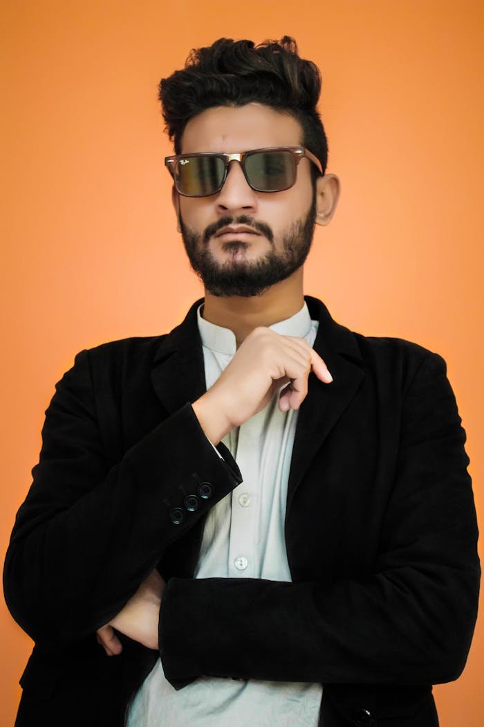 Confident man in sunglasses posing against a vibrant orange backdrop.